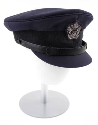 Dark blue peaked cap with silver crest, leather strap and brim displayed atop a mannequin head …