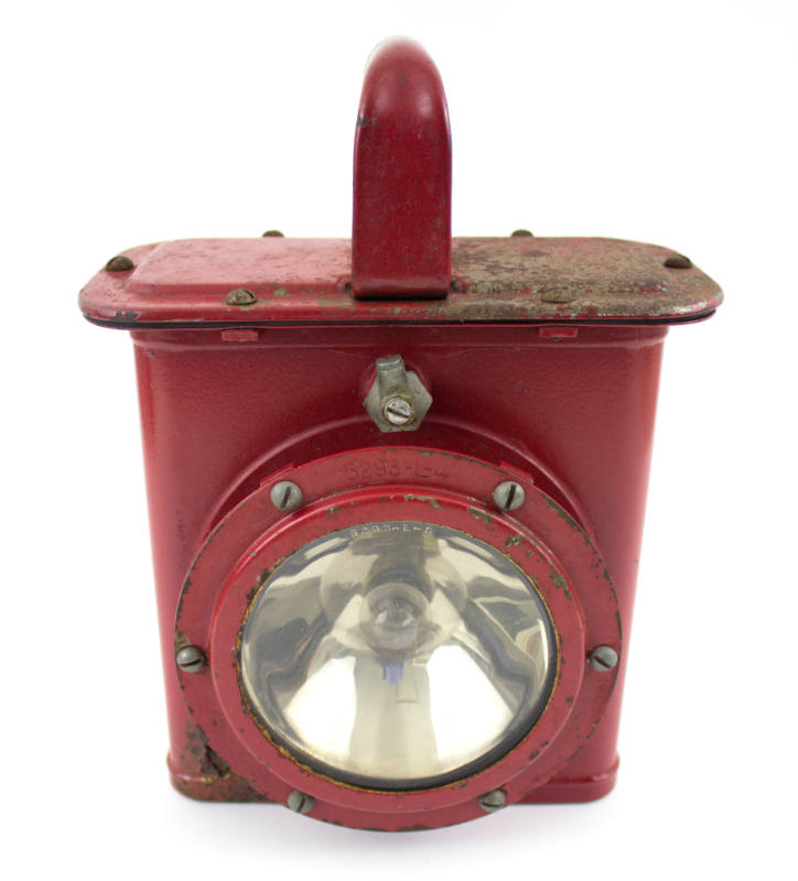 Red metal lantern with red handle on top and round glass plate light on lower center 