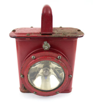Red metal lantern with red handle on top and round glass plate light on lower center 
