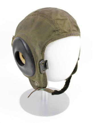 Green fabric helmet with black rubber ear pads and leather chin strap, displayed on mannequin h…