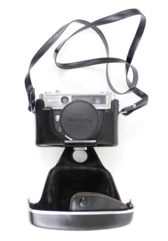 Manual camera inside a black carrying case with attatched neck strap; case is open to show came…