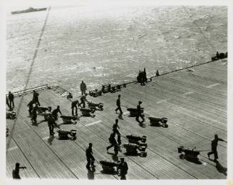 Black and white photograph of men pushing bombs across the flight deck