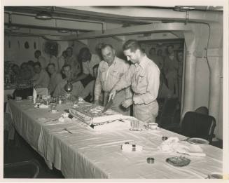 Printed black and white photograph of two officers cutting a cake in Intrepid's wardroom