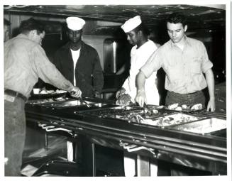 Black and white photograph of four men standing along the chow line, serving Christmas dinner