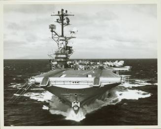 Black and white photograph of USS Intrepid at sea from the bow with aircraft visible on the fli…