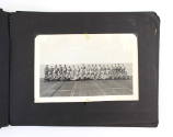 Black scrapbook page open to a black and white photograph showing a division of crew members po…