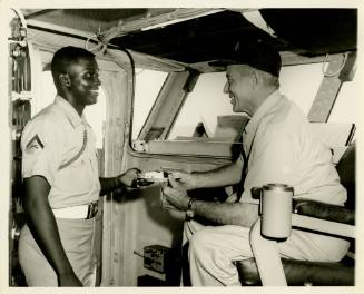 Black and white photograph of a Marine handing a slice of cake to Intrepid's commanding officer…
