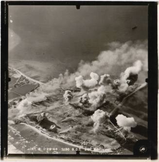 Black and white aerial photograph of Roi Island with smoke rising from bombing locations