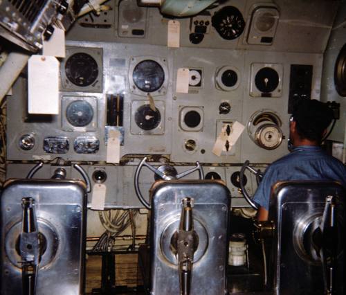 Printed color photograph of USS Growler's control room with a sailor seated at a panel of equip…