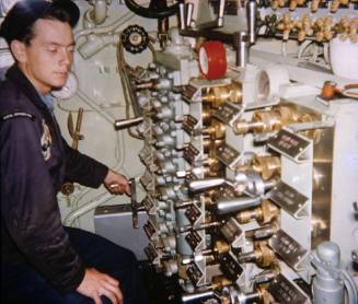 Printed color photograph of a USS Growler crew member sitting in front of the air manifolds in …