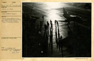 Black and white photograph mounted on paper of multiple crew members on the flight deck near tw…