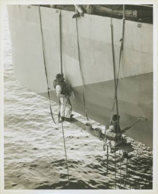 Black and white photograph of two sailors painting the side of USS Intrepid