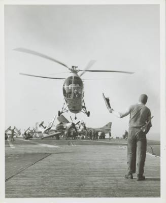 Black and white photograph of Piasecki HUP-2 Retriever above the Flight Deck with a crewmember …