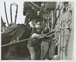 Black and white photograph of a sailor in a hard hat securing a line during refueling