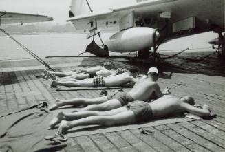 Black and white photograph of men sunbathing on USS Intrepid's flight deck