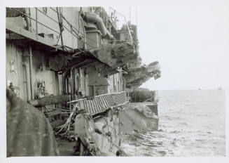 Black and white photograph of damage to the starboard side of the aircraft carrier USS Intrepid…