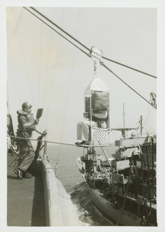 Black and white photograph of a person in a highline chair transferring between ships at sea