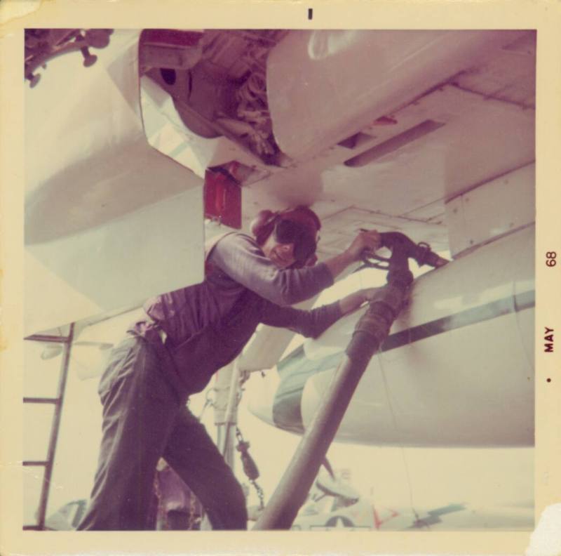 Color photograph of a flight deck crew member refueling an aircraft