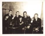 Black and white photograph of four U.S. Navy officers smiling and holding their glasses up to t…