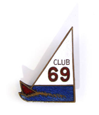 Enamel pin in the shape of a sailboat on blue water with words "Club 69" on sail