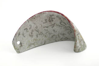 Light gray curved metal fragment with red painted edge and dark scratches throughout
