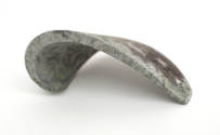 Light gray curved metal fragment with dark scratches throughout, underside view