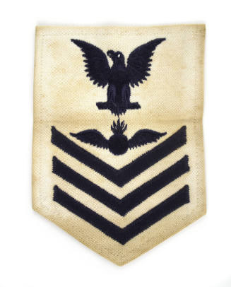 White U.S. Navy uniform patch with dark blue eagle, chevrons and image of a bomb with wings