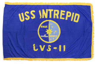 Royal blue flag with fringe on three sides, circular USS Intrepid insignia in center surrounded…