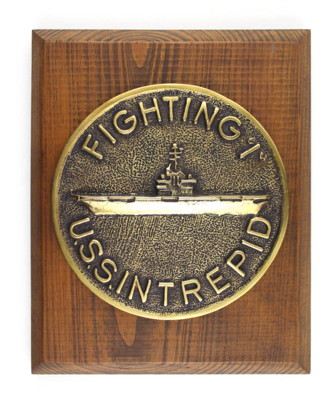 Wooden plaque with circular brass medallion showing an image of the aircraft carrier USS Intrep…