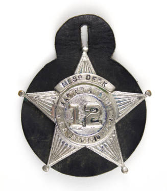 Silver badge in the shape of five pointed star with black circular backing, inscription reads “…