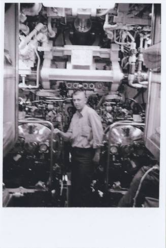 Black and white image of David E. Bishop standing between two torpedo tubes inside submarine US…