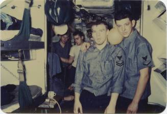Colored image of two men standing next to each other in USS Growler berthing area with orange b…