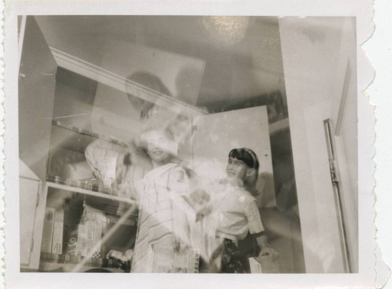 Black and white double exposed image of two girls standing in front of an open food cupboard