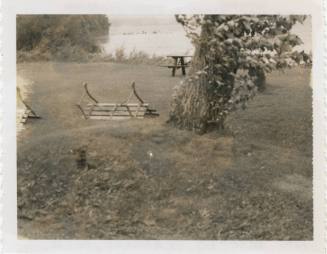 Black and white image of benches knocked over during a storm, tree trunk with greenery in cente…