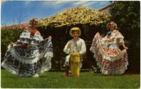 Printed postcard with color photograph of two women dancing with a man playing the drums in bet…