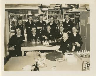 Black and white image of officers and enlisted men around a table in USS Intrepid's library wit…