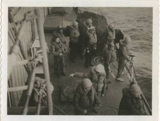 Black and white image of enlisted men in life jackets and hard hats at the edge of the deck