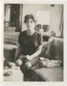 Black and white image a woman sitting on a sofa with two dolls next to her, a tufted chair and …