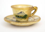 Miniature teacup set on top of a saucer, cup depicts hand painted landscape scene of Mount Fuji
