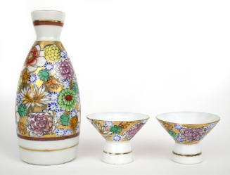 Sake set including a bottle standing next to two wide-mouth cups with colored floral motif 