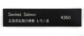Black restaurant sign with English and Japanese characters advertising smoked salmon