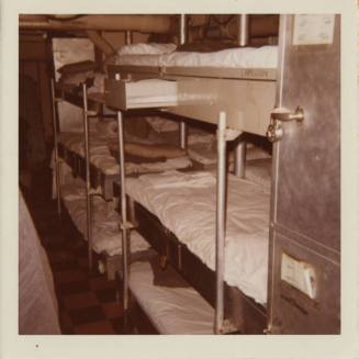 Color photograph of a sleeping compartment with metal bunks stacked three high and metal locker…