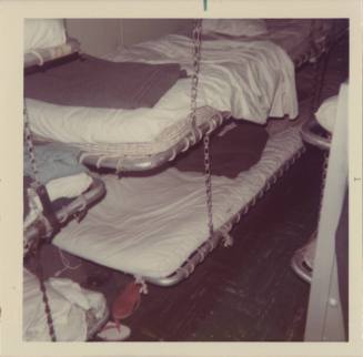 Color photograph of a sleeping compartment with stacked bunks with white sheets and gray blanke…