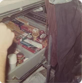 Color photograph of cookies, candies, crackers and other snacks stored in a locker under a bunk…