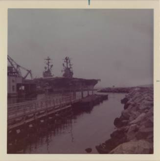 Color photograph of two aircraft carriers in port in Quonset Point, Rhode Island, with pier and…