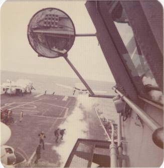 Color photograph of USS Intrepid's flight deck taken from the island, with a rearview mirror in…