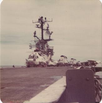 Color photograph of Intrepid's flight deck with a Sikorsky SH-3 Sea King helicopter parked in t…