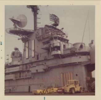 Color photograph of USS Intrepid's island, with yellow aircraft carts parked in front of it