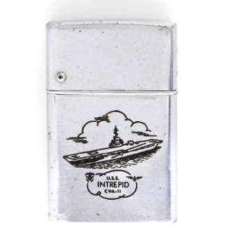 Silver lighter with engraved image of an aircraft carrier in front of a large cloud, inscriptio…