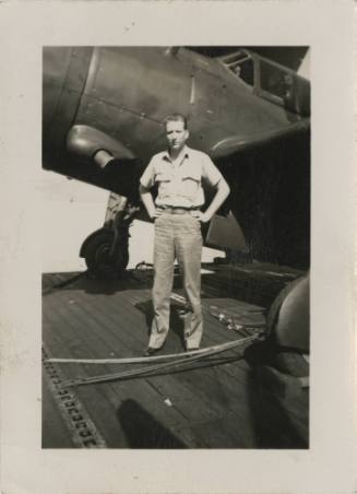 Black and white photograph of a man standing next to a Curtiss SB2C Helldiver on the flight dec…